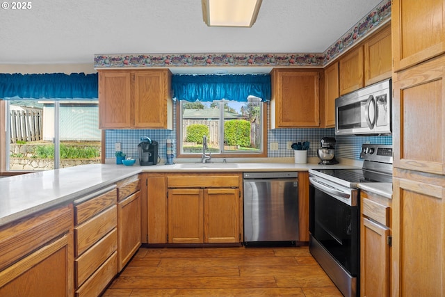 kitchen with appliances with stainless steel finishes, wood finished floors, light countertops, and a sink