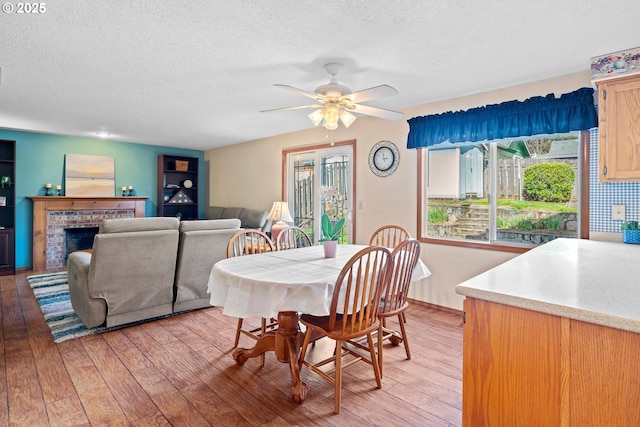 dining space featuring a ceiling fan, a textured ceiling, a fireplace, and light wood finished floors