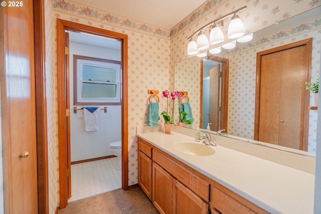 bathroom with baseboards, toilet, vanity, and wallpapered walls