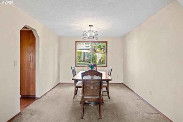 dining area featuring arched walkways, light colored carpet, an inviting chandelier, and a textured ceiling