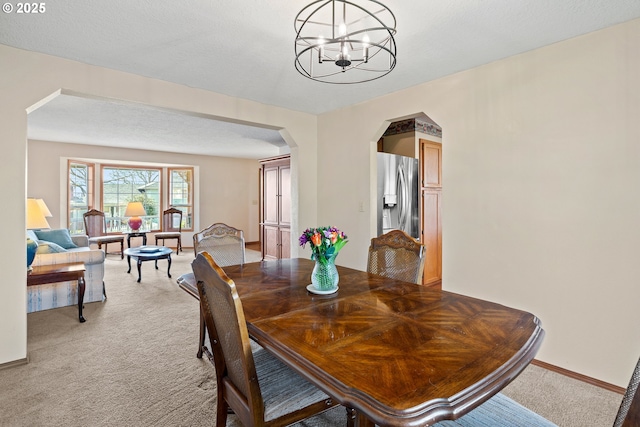 dining area featuring baseboards, a chandelier, light carpet, arched walkways, and a textured ceiling