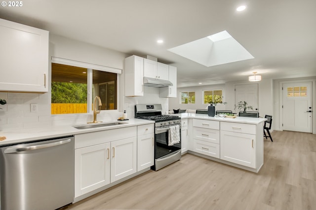 kitchen featuring under cabinet range hood, stainless steel appliances, a sink, a skylight, and a peninsula