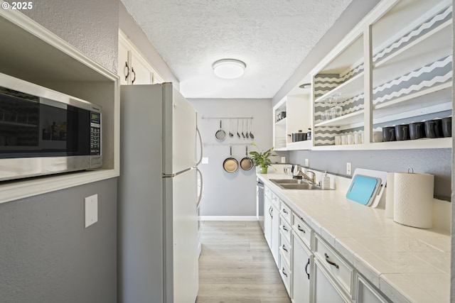 kitchen featuring a textured ceiling, sink, light hardwood / wood-style flooring, white cabinets, and white fridge