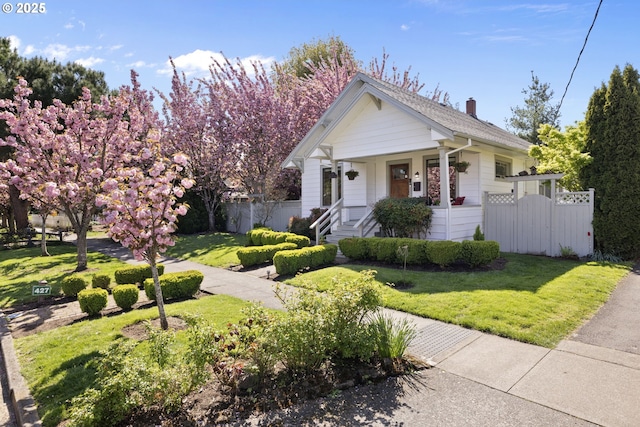 view of front facade featuring fence, a chimney, a porch, and a front yard