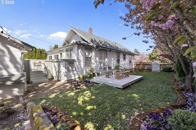 back of property featuring a yard, a deck, fence, and a chimney