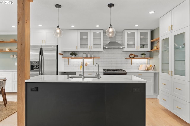 kitchen featuring open shelves, wall chimney range hood, appliances with stainless steel finishes, light wood-style floors, and a sink