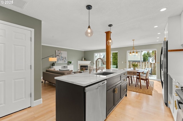 kitchen featuring light wood finished floors, a center island with sink, a fireplace, stainless steel appliances, and a sink