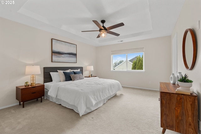 bedroom with a raised ceiling, light colored carpet, and baseboards