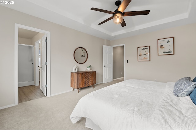 bedroom with baseboards, a tray ceiling, ceiling fan, light carpet, and connected bathroom