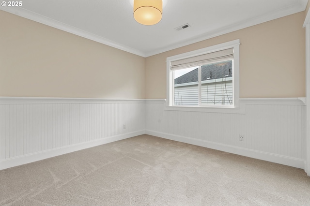 carpeted spare room featuring a wainscoted wall, visible vents, and ornamental molding