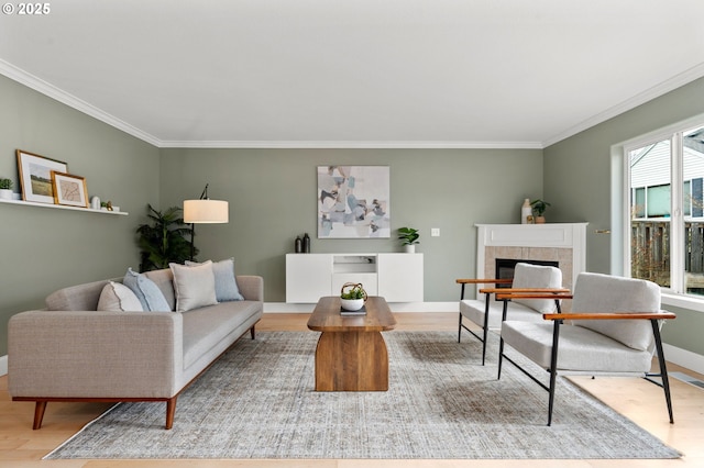 living area with ornamental molding, a tile fireplace, baseboards, and wood finished floors