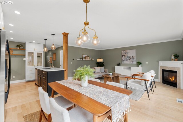 dining room featuring light wood finished floors, crown molding, baseboards, recessed lighting, and a tile fireplace