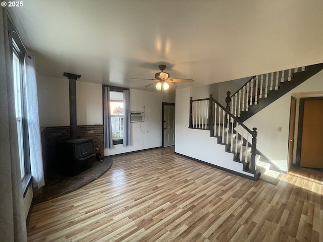 unfurnished living room featuring ceiling fan, light hardwood / wood-style floors, a wall unit AC, and a wood stove