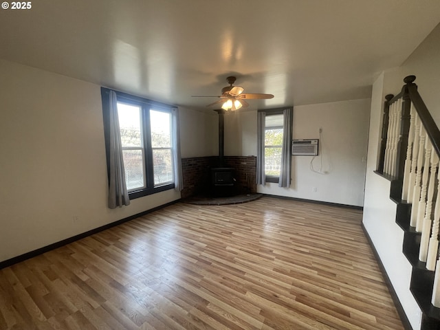 unfurnished living room featuring wood-type flooring, a wood stove, a wall mounted AC, and ceiling fan