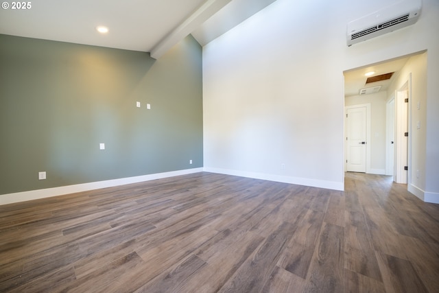 unfurnished room featuring a towering ceiling, baseboards, an AC wall unit, dark wood finished floors, and attic access