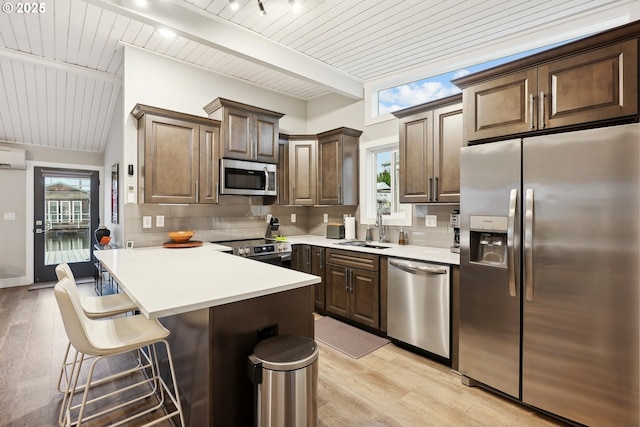 kitchen featuring sink, appliances with stainless steel finishes, beamed ceiling, light hardwood / wood-style floors, and a breakfast bar area