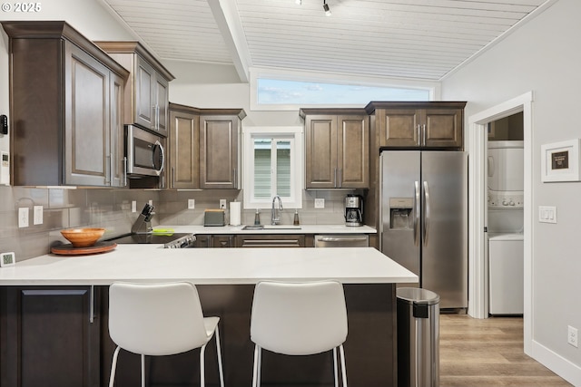 kitchen with tasteful backsplash, stacked washing maching and dryer, sink, and stainless steel appliances