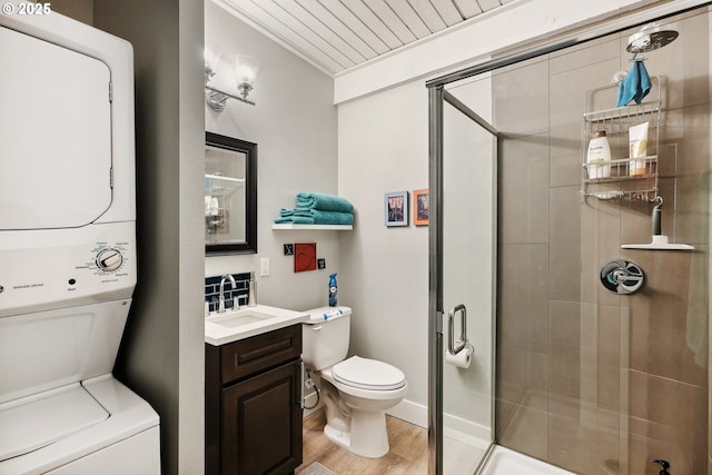 bathroom featuring walk in shower, stacked washer / dryer, toilet, vanity, and hardwood / wood-style flooring