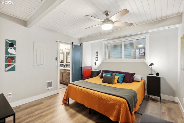 bedroom with ensuite bath, hardwood / wood-style flooring, ceiling fan, a barn door, and beam ceiling