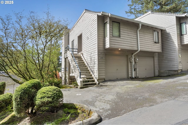 view of side of home featuring an attached garage, a chimney, stairway, and aphalt driveway