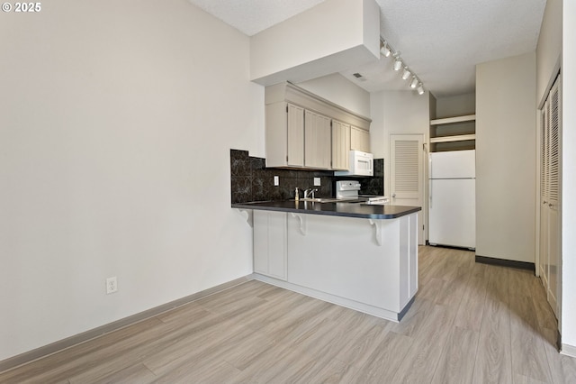 kitchen with dark countertops, light wood-style floors, white appliances, a peninsula, and decorative backsplash