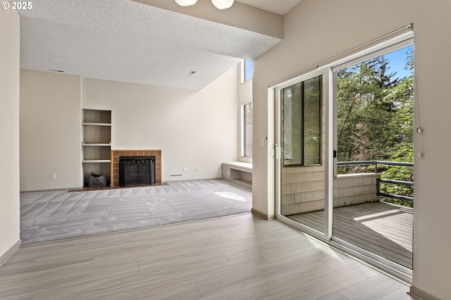unfurnished living room with baseboards, a textured ceiling, a tiled fireplace, and wood finished floors
