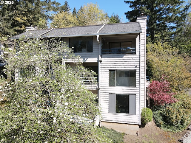 view of side of home with a chimney, a balcony, and roof with shingles