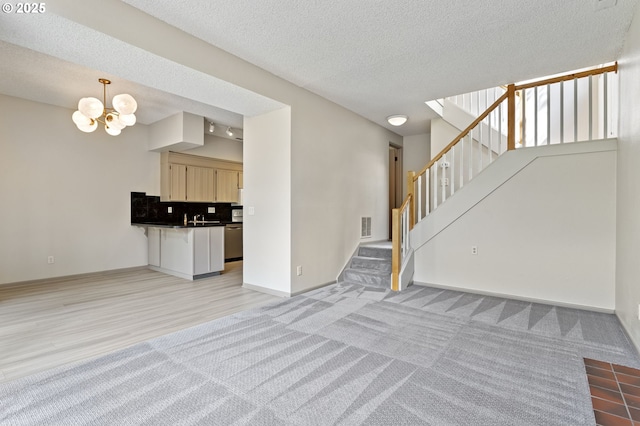 unfurnished living room featuring a textured ceiling, light colored carpet, visible vents, an inviting chandelier, and stairs
