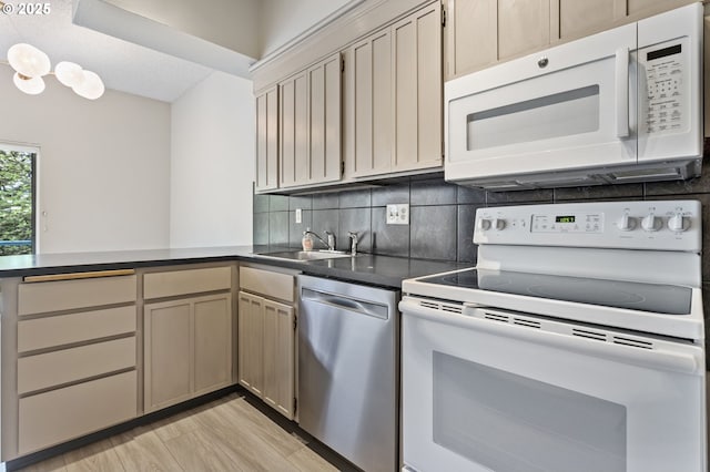 kitchen with dark countertops, a sink, white appliances, a peninsula, and tasteful backsplash