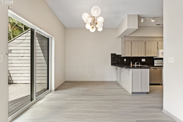 kitchen featuring a peninsula, dark countertops, white microwave, backsplash, and a notable chandelier