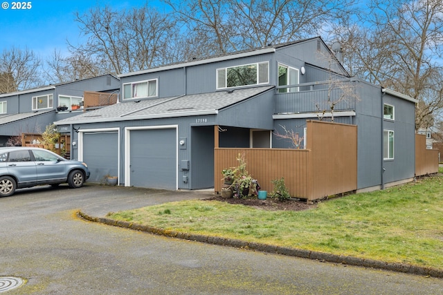 view of property featuring a garage, roof with shingles, a front lawn, and aphalt driveway