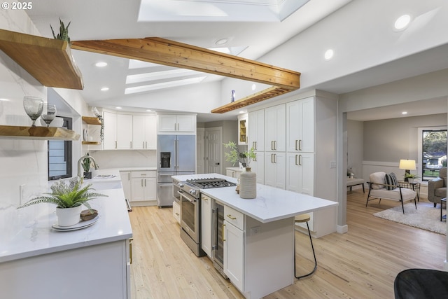 kitchen featuring stainless steel appliances, vaulted ceiling with skylight, a kitchen island, light wood-type flooring, and white cabinets