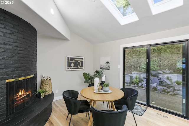 dining area featuring lofted ceiling with skylight, a fireplace, and light wood-type flooring