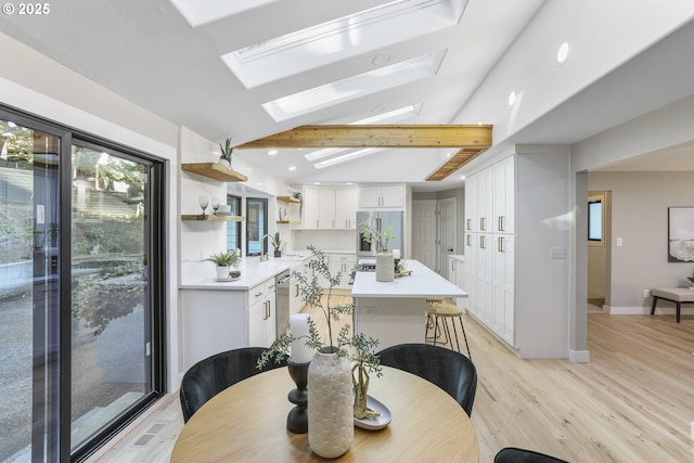 dining space with light hardwood / wood-style floors, vaulted ceiling with skylight, and sink