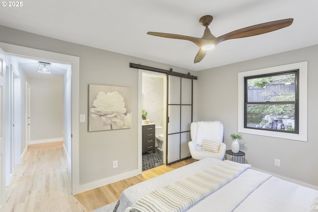 bedroom with ensuite bathroom, light wood-type flooring, ceiling fan, and a barn door