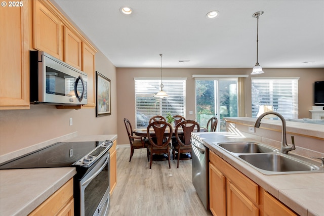 kitchen featuring light brown cabinetry, light wood finished floors, stainless steel appliances, and a sink