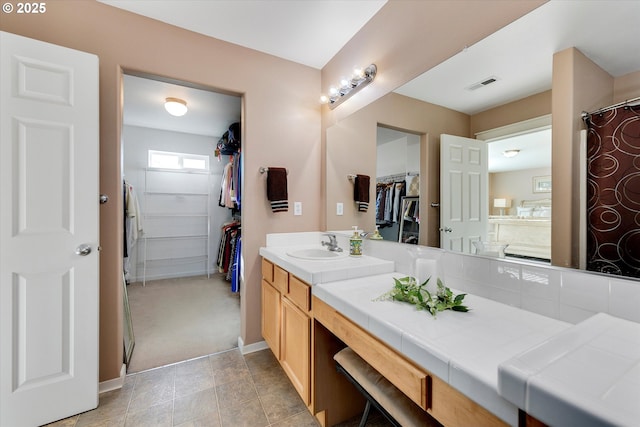 bathroom featuring visible vents, vanity, a walk in closet, and baseboards