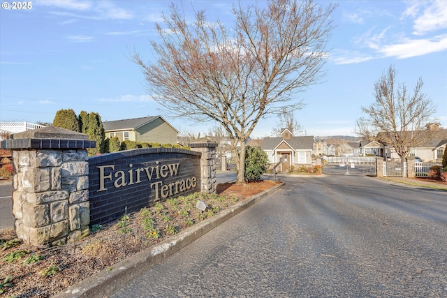 community / neighborhood sign featuring a gate, fence, a residential view, and driveway