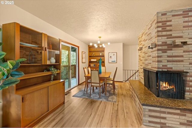 4819 SW Hamilton St, Portland, OR 97221 - dining room with light wood-type flooring, a chandelier, a textured ceiling, and a multi sided fireplace