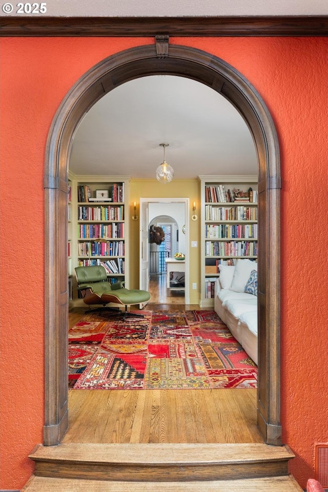 living area featuring a textured wall, baseboards, built in features, and arched walkways