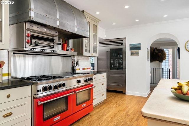 kitchen featuring decorative backsplash, light wood-style flooring, custom range hood, ornamental molding, and high end appliances