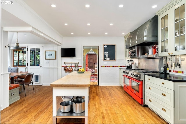 kitchen featuring double oven range, wall chimney range hood, open shelves, light wood-style flooring, and ornamental molding