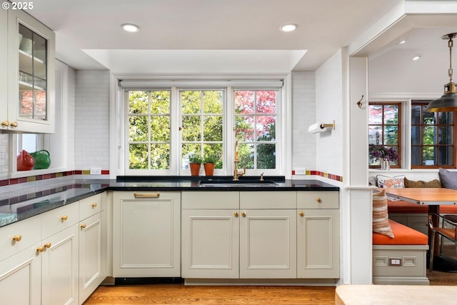 kitchen featuring glass insert cabinets, light wood-style flooring, a sink, and a wealth of natural light