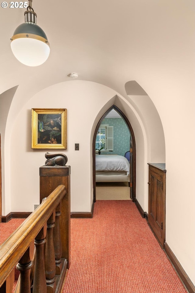 hallway with carpet floors, baseboards, and arched walkways