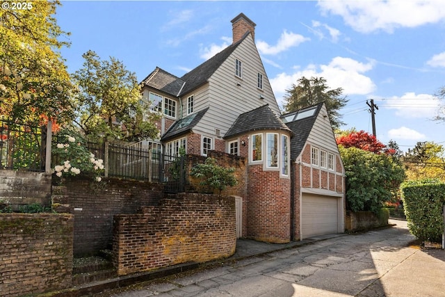 view of home's exterior featuring a chimney, brick siding, fence, a garage, and driveway