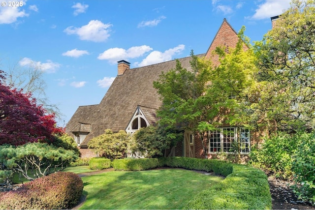 view of side of home featuring a chimney, brick siding, and a yard