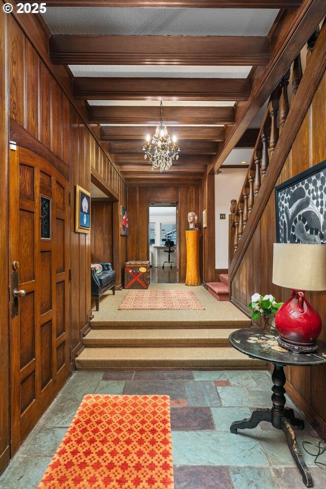 foyer entrance featuring stairs, carpet floors, a chandelier, beamed ceiling, and wood walls