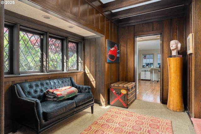 sitting room featuring beam ceiling, wood walls, and light colored carpet