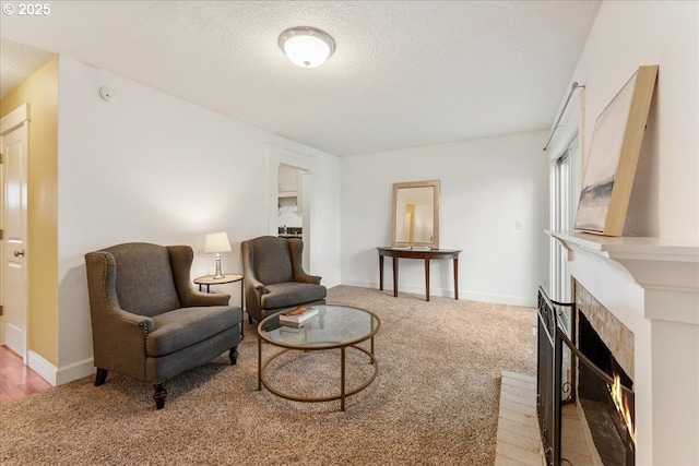 living area with a warm lit fireplace, a textured ceiling, baseboards, and carpet floors