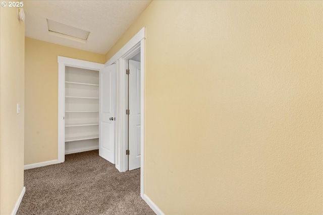 hallway featuring baseboards, attic access, and carpet